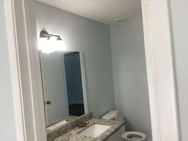 a bathroom with a granite countertop sink a toilet and a mirror