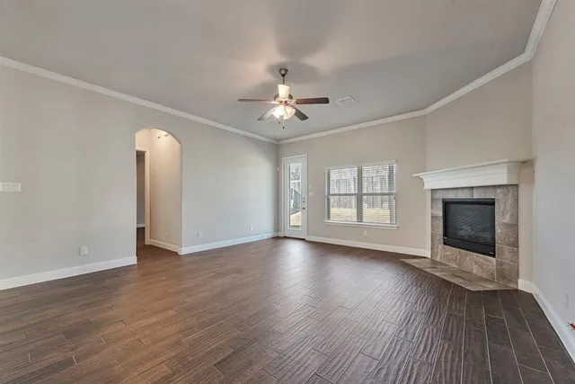an empty room with large windows a fireplace a ceiling fan and wooden floor