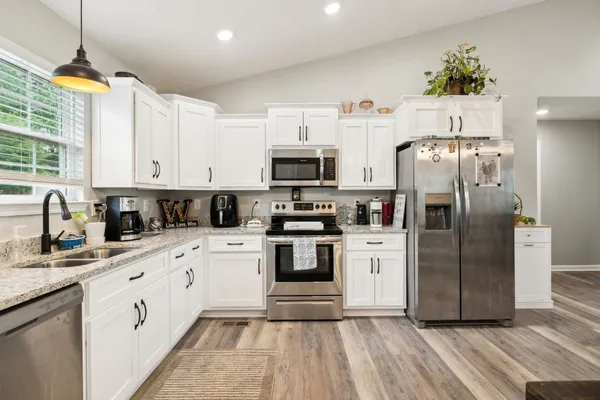 a kitchen with granite countertop a refrigerator oven a sink dishwasher and white cabinets with wooden floor