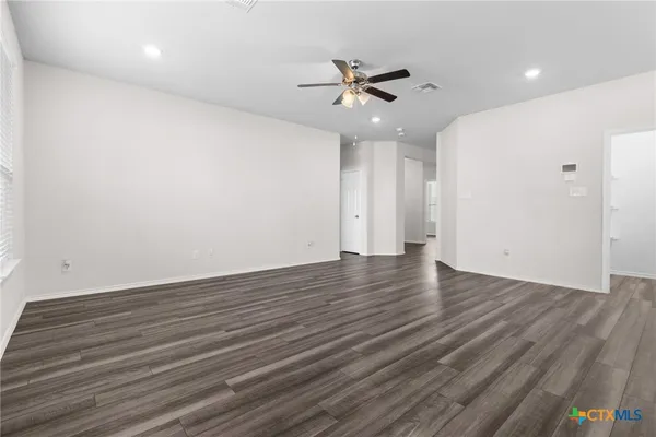 a view of an empty room with wooden floor and a ceiling fan