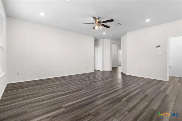 a view of an empty room with wooden floor and a ceiling fan
