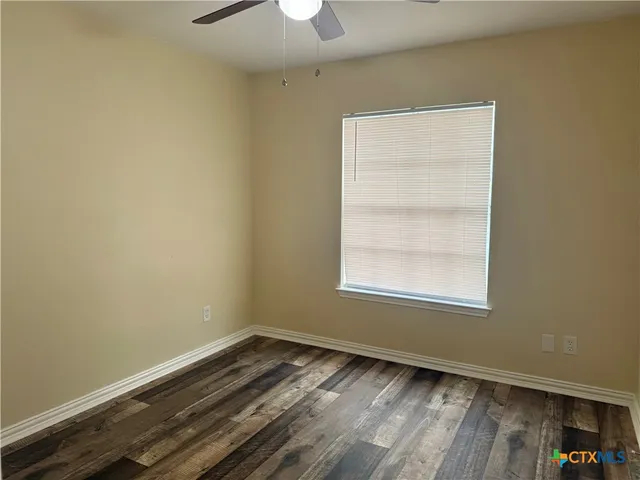 an empty room with wooden floor chandelier fan and windows