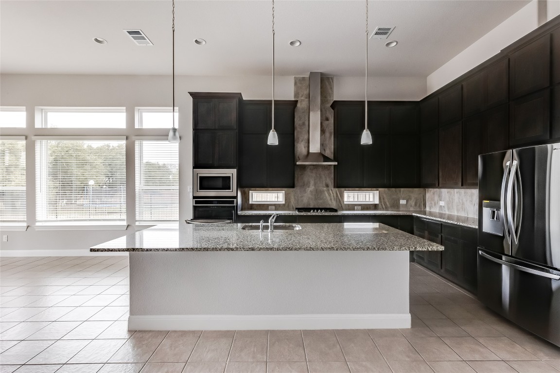 1948 Equine Road Leander, TX 78641 - Photo 12 of 36 Kitchen featuring decorative backsplash, stainless steel appliances, light stone counters, hanging light fixtures, and wall chimney range hood
