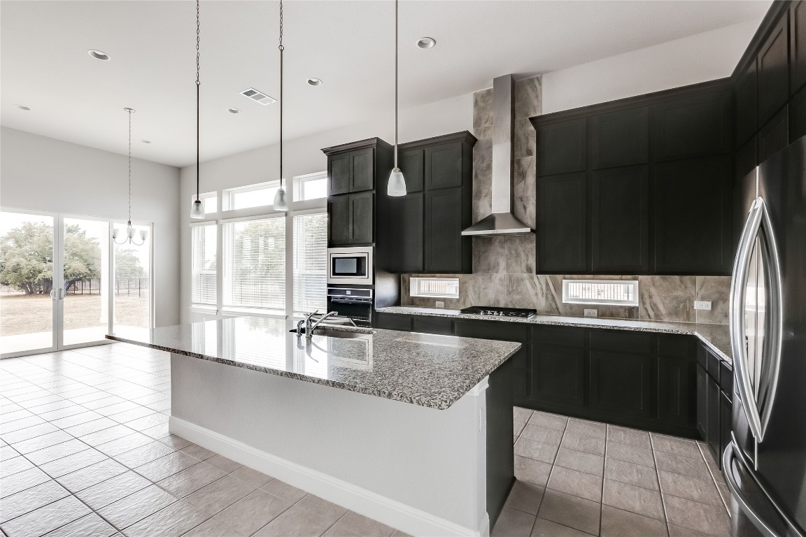 1948 Equine Road Leander, TX 78641 - Photo 13 of 36 Kitchen with dark cabinetry, light stone counters, decorative light fixtures, and recessed lighting