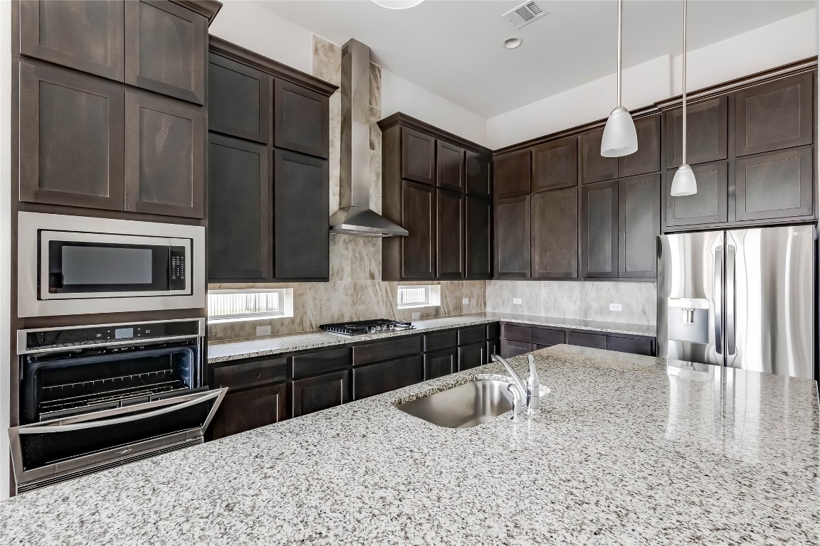 1948 Equine Road Leander, TX 78641 - Photo 14 of 36 Kitchen featuring appliances with stainless steel finishes, dark brown cabinetry, pendant lighting, and tasteful backsplash