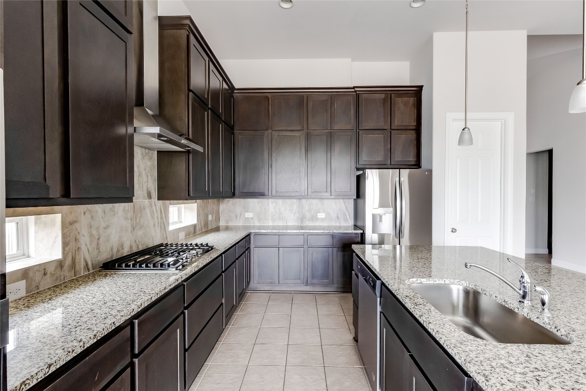 1948 Equine Road Leander, TX 78641 - Photo 15 of 36 Kitchen featuring light stone counters, dark brown cabinets, decorative backsplash, stainless steel appliances, and pendant lighting
