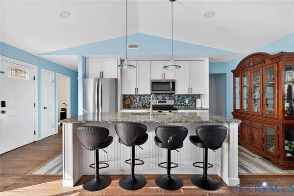 a kitchen with stainless steel appliances granite countertop a stove a sink a refrigerator cabinets and chairs with wooden floor