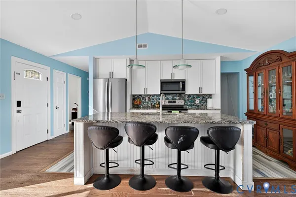 a kitchen with stainless steel appliances granite countertop a refrigerator a stove a sink white cabinets with chairs and white cabinets