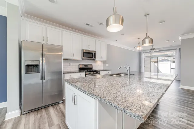 a kitchen with stainless steel appliances granite countertop a stove top oven a sink a dining table and chairs with white cabinets