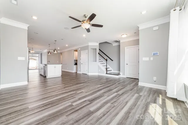 a view of an empty room with wooden floor ceiling fan and windows