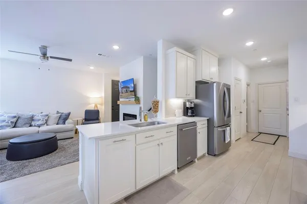 a large white kitchen with stainless steel appliances granite countertop a stove a sink a refrigerator and white cabinets with wooden floor