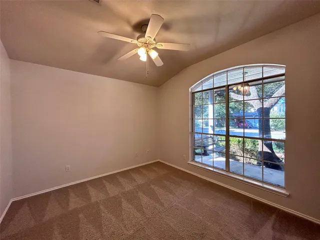 an empty room with chandelier fan and windows