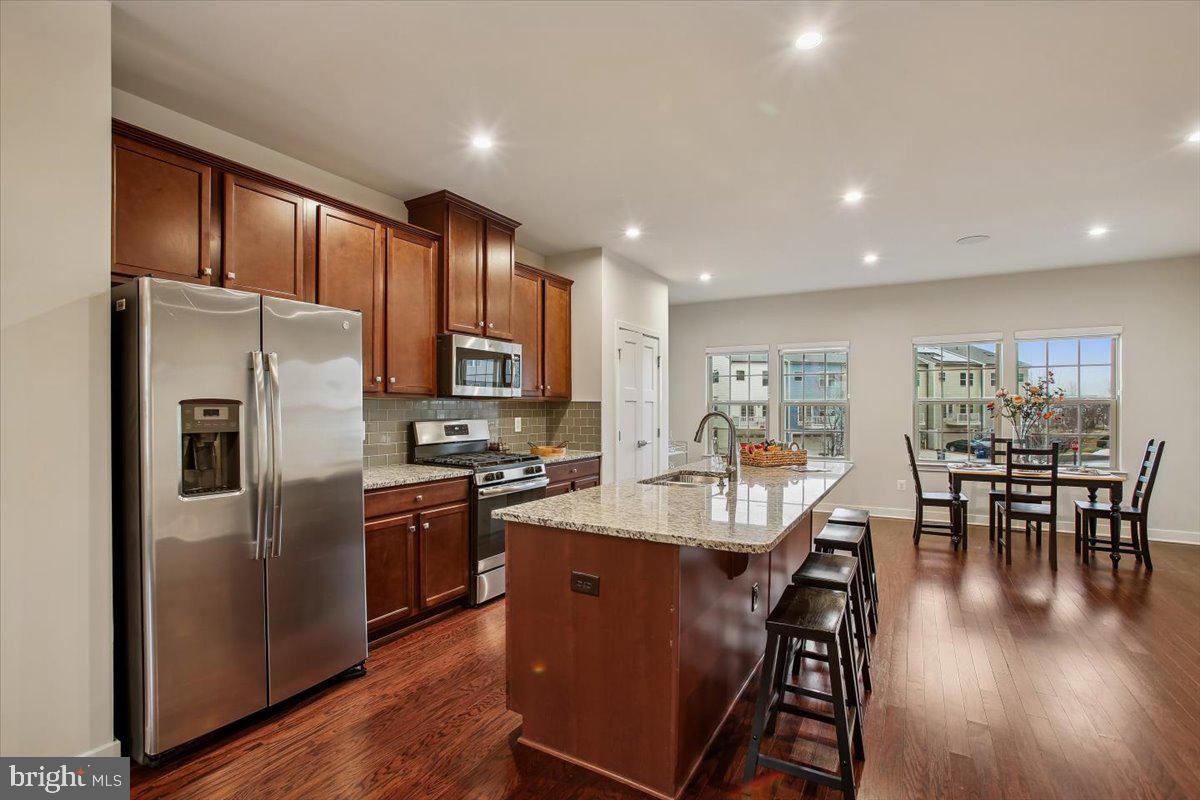 2105 Hemlock Bay Road Dumfries, VA 22026 - Photo 4 of 48 a kitchen with stainless steel appliances granite countertop a refrigerator a stove top oven a dining table and chairs with wooden floor