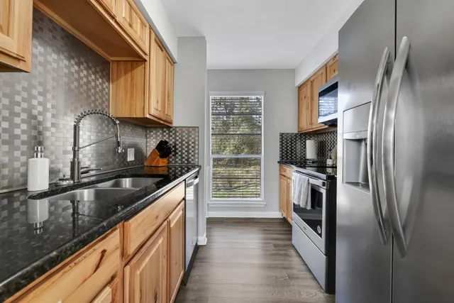 a kitchen with stainless steel appliances granite countertop a refrigerator a stove and a sink with wooden floor
