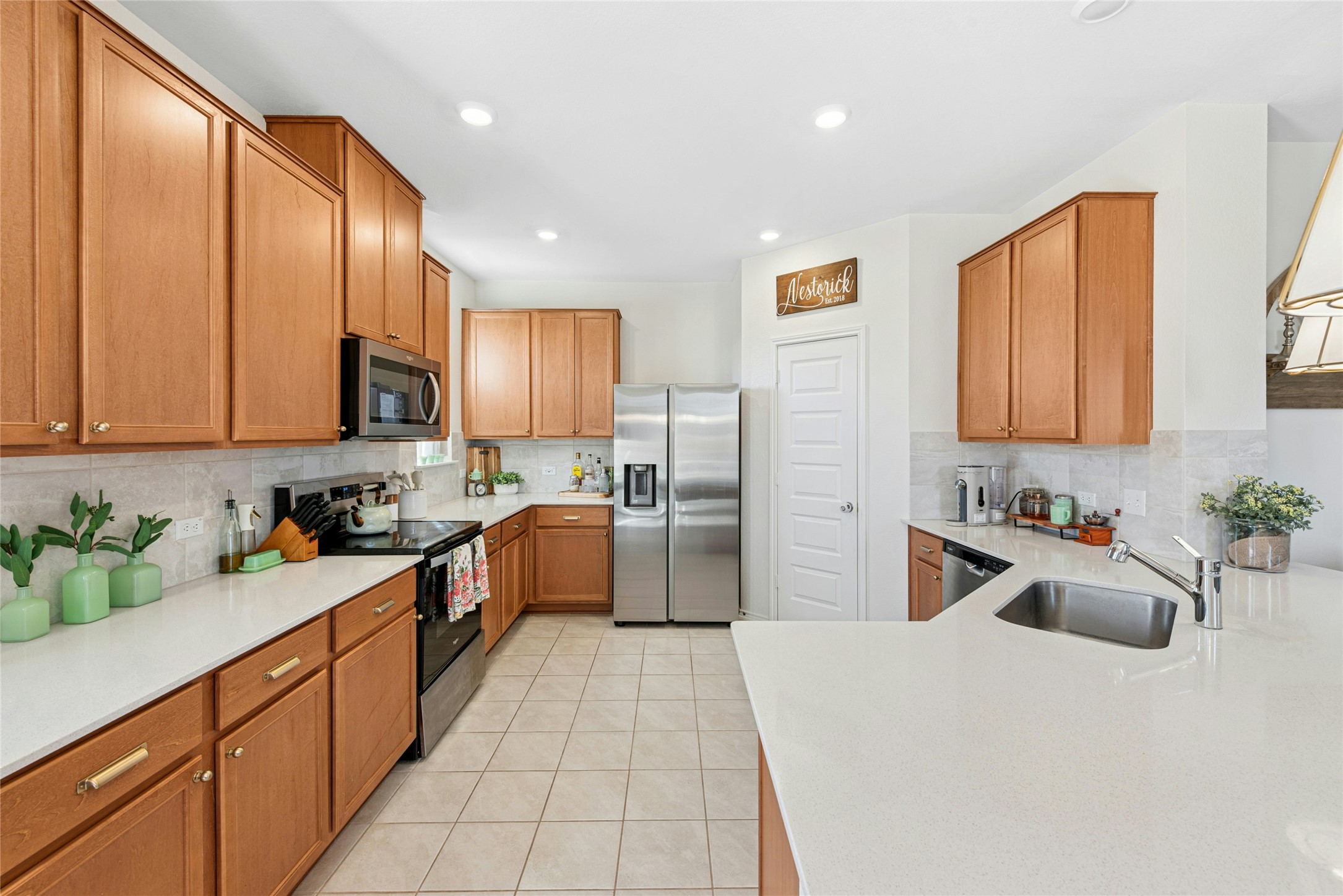 2001 Saskatoon Street Georgetown, TX 78626 - Photo 17 of 40 The kitchen features warm wood-finish cabinets, sleek stainless steel appliances, light tile-patterned flooring, a functional peninsula for additional workspace, and a stylish decorative backsplash that adds the perfect finishing touch. Beautiful natural quartz stone countertops enhance the surfaces throughout, adding both durability and refined elegance to the home.
