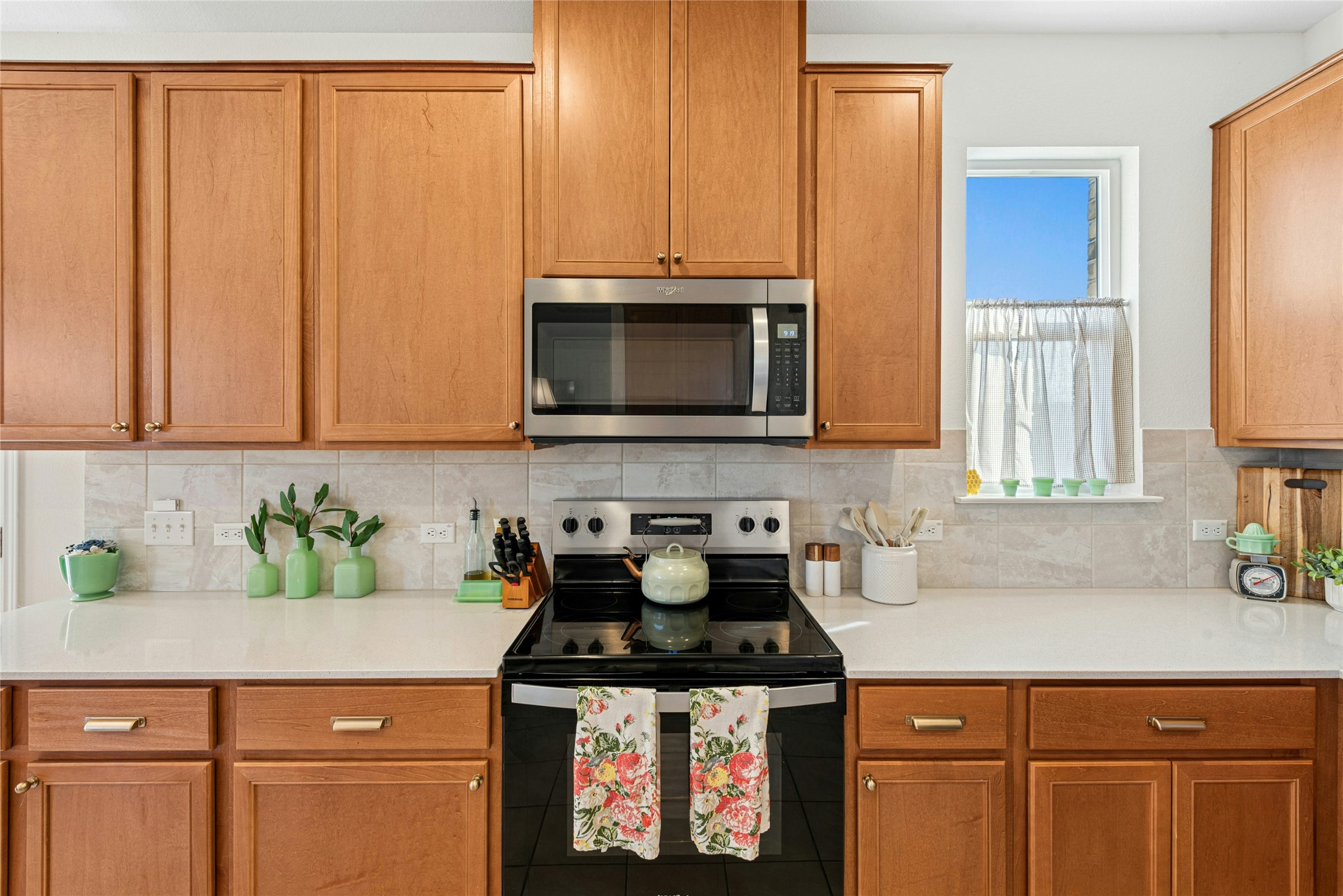 2001 Saskatoon Street Georgetown, TX 78626 - Photo 20 of 40 Kitchen featuring range with electric cooktop, stainless steel microwave, backsplash, and wood finish cabinetry. Beautiful natural quartz stone countertops enhance the surfaces throughout, adding both durability and refined elegance to the home.