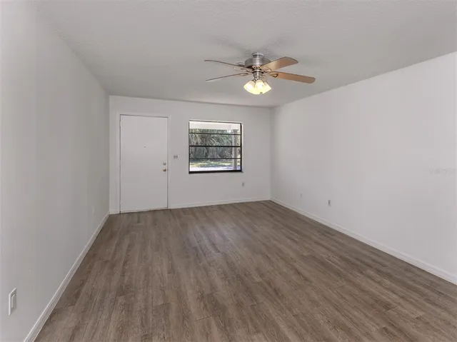 an empty room with wooden floor chandelier fan and windows