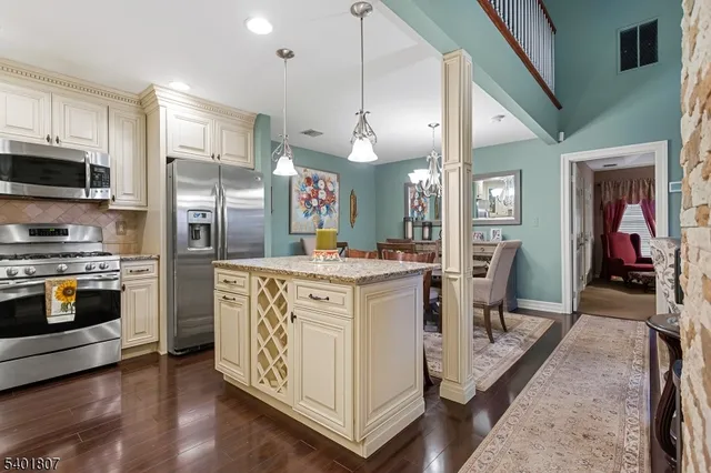 a kitchen with stainless steel appliances kitchen island granite countertop a refrigerator a stove top oven a sink dishwasher and white cabinets with wooden floor