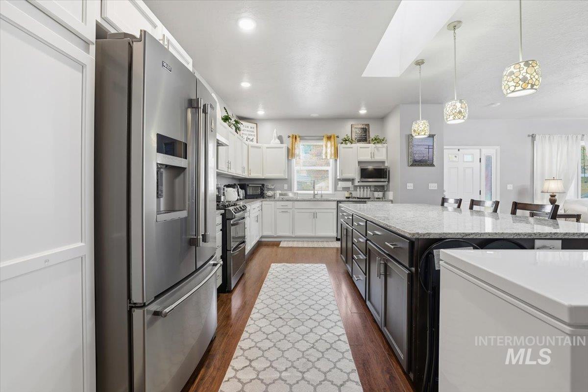 7501 West Swift Lane Boise, ID 83704 - Photo 13 of 50 Kitchen with appliances with stainless steel finishes, white cabinets, dark wood-style floors, a kitchen breakfast bar, and decorative light fixtures
