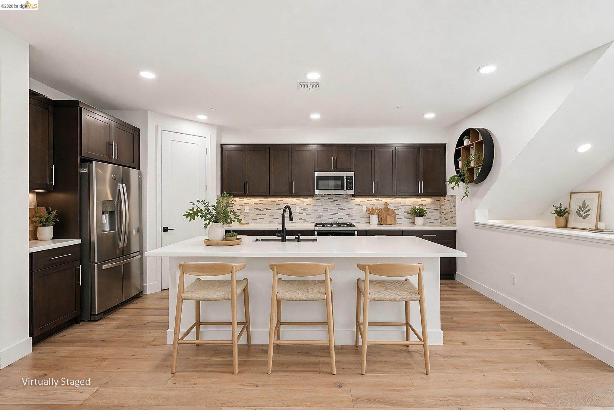 18210 Argento Loop San Ramon, CA 94583 - Photo 9 of 44 Modern kitchen featuring wood-finish flooring, dark wood cabinetry, stainless steel appliances, a tile backsplash, and a white countertop island with seating