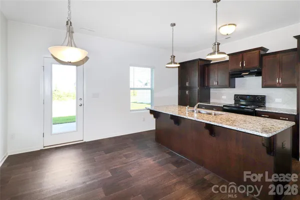 a kitchen with stainless steel appliances granite countertop a stove a sink a refrigerator and a wooden floor