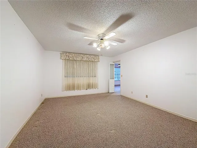 an empty room with chandelier fan and windows