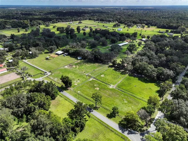 an aerial view of a residential houses with outdoor space and trees all around