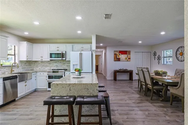 a living room with stainless steel appliances furniture dining table and wooden floor