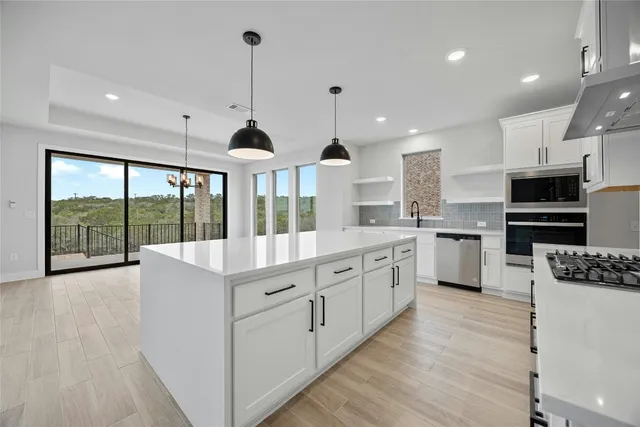 a large kitchen with stainless steel appliances kitchen island granite countertop a stove a sink a refrigerator and white cabinets with wooden floor