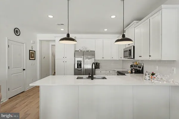 a kitchen with stainless steel appliances granite countertop a sink a refrigerator a stove and white cabinets with wooden floor