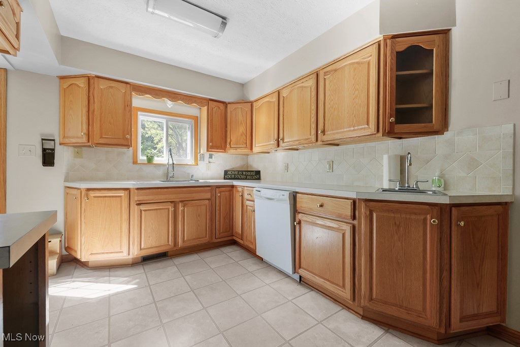 1702 Far View Road Akron, OH 44312 - Photo 12 of 49 Kitchen with light countertops, light tile patterned floors, backsplash, dishwasher, and glass insert cabinets