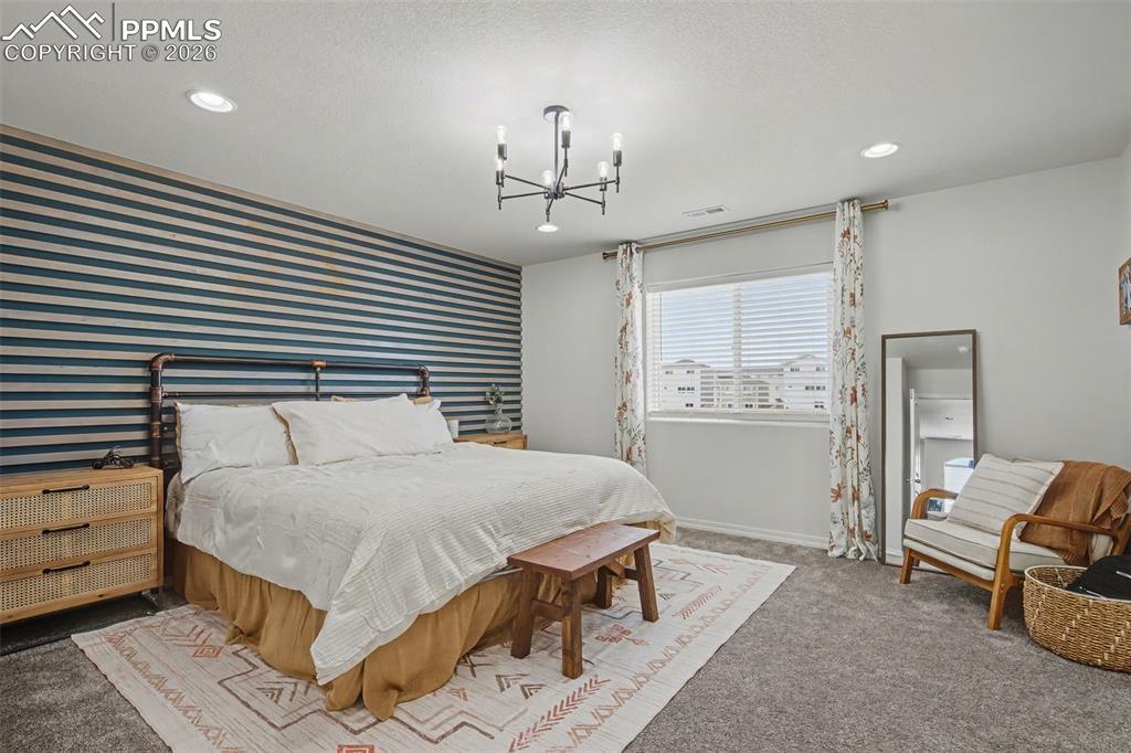 7811 Berwyn Loop Peyton, CO 80831 - Photo 23 of 38 a spacious bedroom with a bed a chandelier and mirror