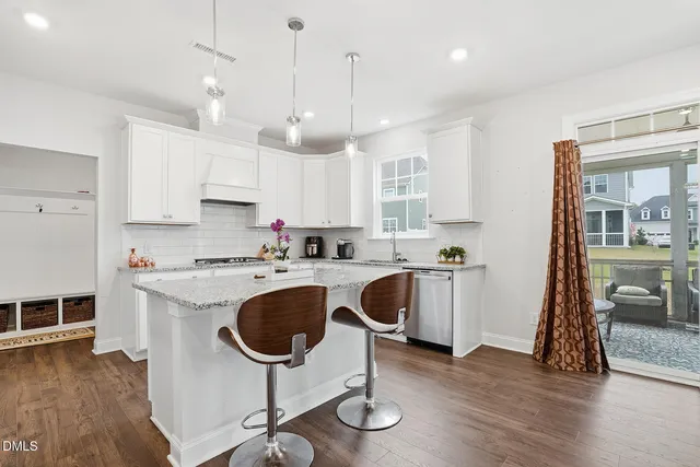 a kitchen with kitchen island granite countertop a sink a stove a refrigerator and white cabinets with wooden floor