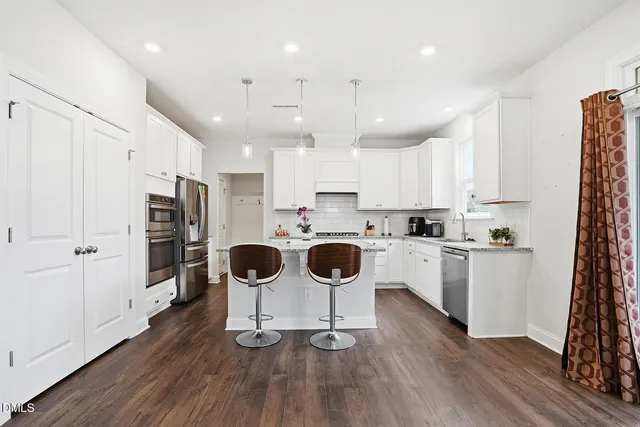 a kitchen with stainless steel appliances a refrigerator a stove top oven a sink dishwasher and white cabinets with wooden floor