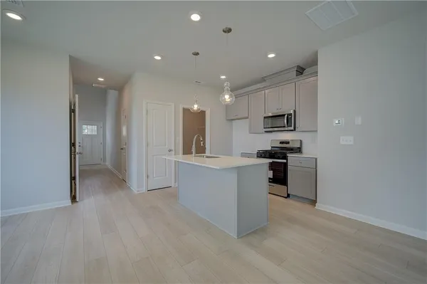 a view of kitchen with stainless steel appliances refrigerator oven and white cabinets with wooden floor