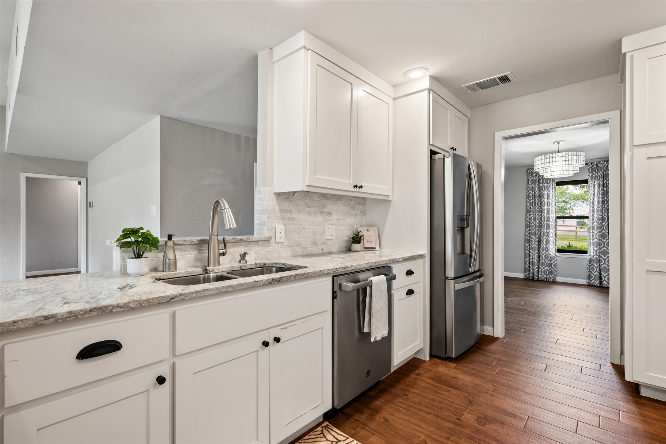 1600 Pin Oak Lane Round Rock, TX 78681 - Photo 22 of 40 Kitchen featuring white shaker cabinetry with black hardware, light granite countertops, a stainless steel double basin sink with a gooseneck faucet, and a stone-look tile backsplash