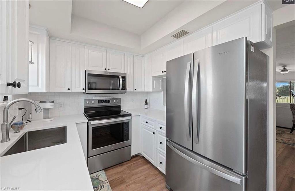 476 Bristle Cone Lane, Unit 39 Naples, FL 34113 - Photo 2 of 16 Kitchen with stainless steel appliances, white cabinetry, light wood-type flooring, backsplash, and light stone countertops