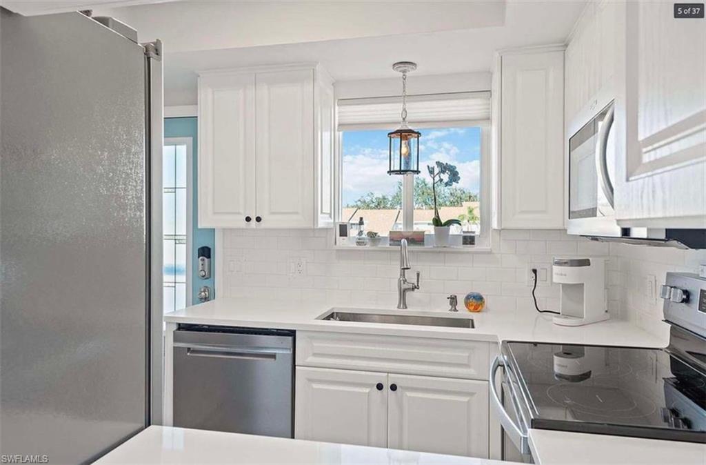 476 Bristle Cone Lane, Unit 39 Naples, FL 34113 - Photo 3 of 16 Kitchen featuring stainless steel appliances, white cabinetry, decorative light fixtures, light stone counters, and tasteful backsplash