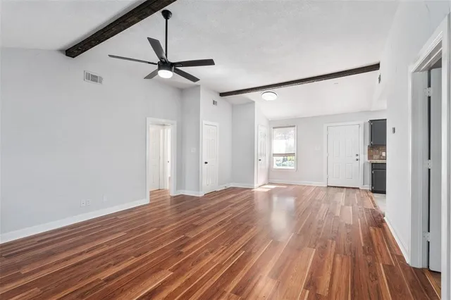 a view of an empty room with wooden floor and a ceiling fan
