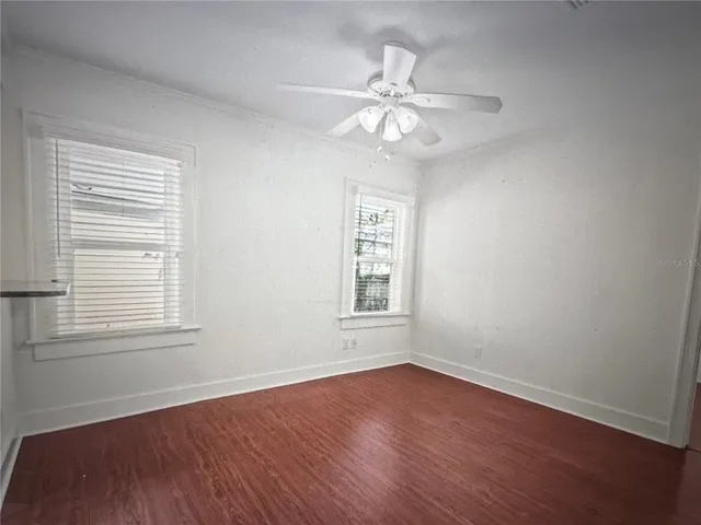 a view of an empty room with wooden floor and a ceiling fan