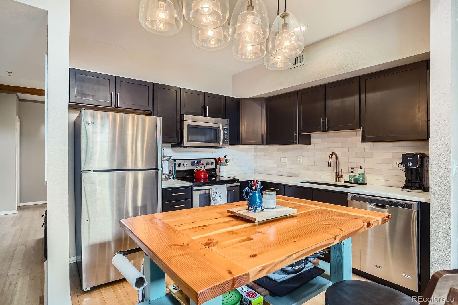 3295 Blake Street, Unit 202 Denver, CO 80205 - Photo 13 of 39 a kitchen with stainless steel appliances granite countertop a refrigerator a sink dishwasher a stove top oven a kitchen island and chairs with wooden floor