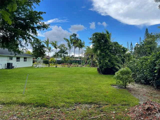 a view of a white house in a big yard with palm trees
