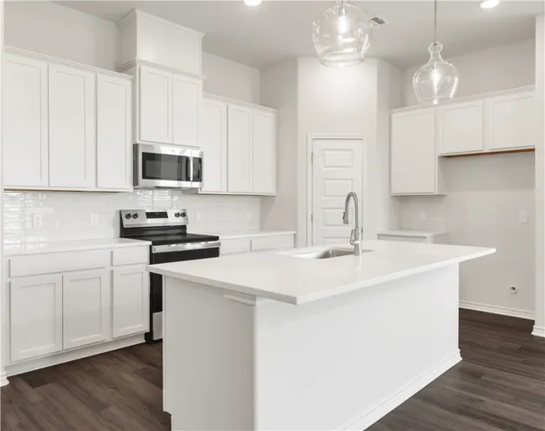 a kitchen with stainless steel appliances a sink a stove a microwave a center island and cabinets