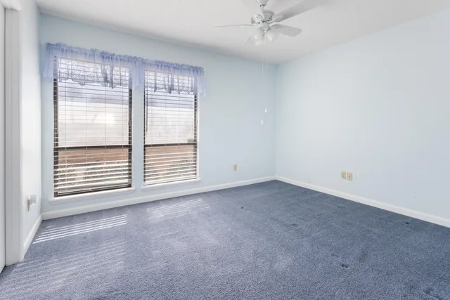 an empty room with a chandelier fan and windows