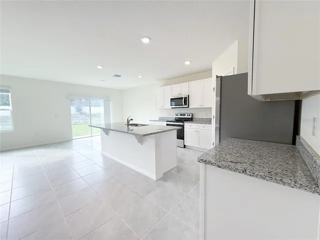 a large white kitchen with kitchen island a stove a sink a refrigerator and white cabinets with wooden floor