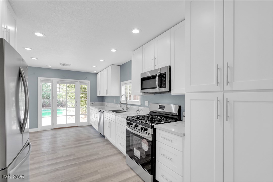 2716 Knightsbridge Road Henderson, NV 89074 - Photo 12 of 27 Kitchen with stainless steel appliances, white cabinets, light wood-type flooring, recessed lighting, and light stone countertops