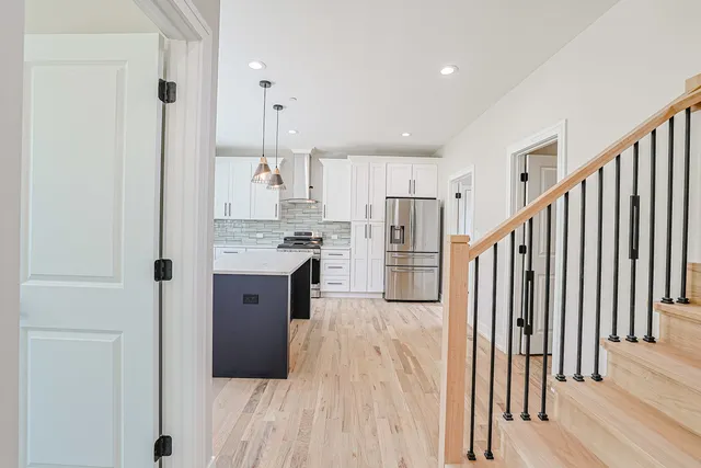 a kitchen with stainless steel appliances granite countertop a refrigerator a oven a sink and white cabinets with wooden floor