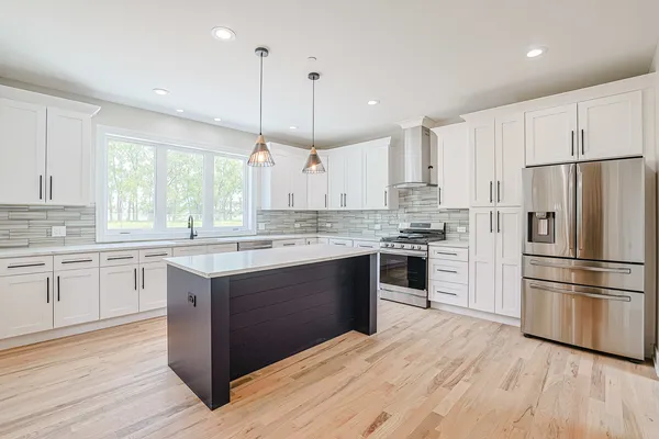 a kitchen with kitchen island granite countertop a refrigerator a sink dishwasher a stove and white cabinets with wooden floor