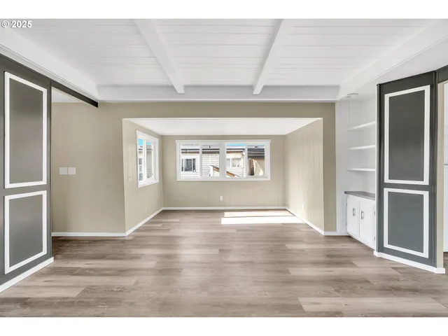 an empty room with wooden floor kitchen view and windows