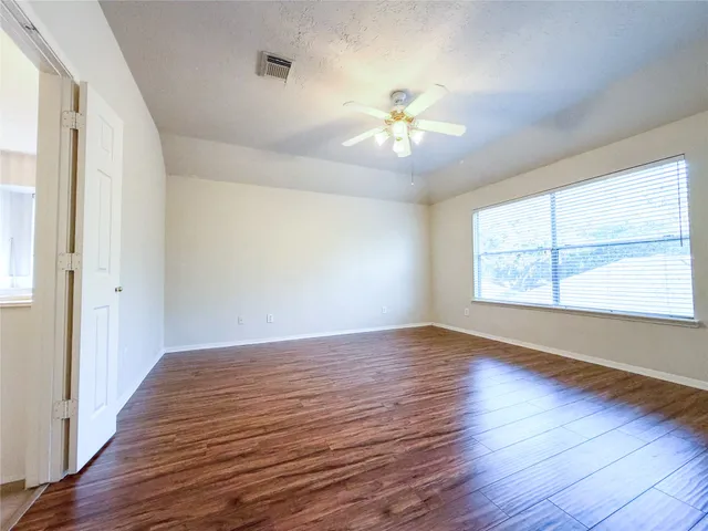 an empty room with wooden floor chandelier fan and windows